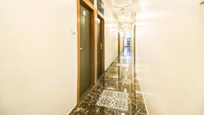 A hallway with marble flooring, wooden doors, and a modern light fixture. - New Axis By Glitz Hotels (Mumbai)