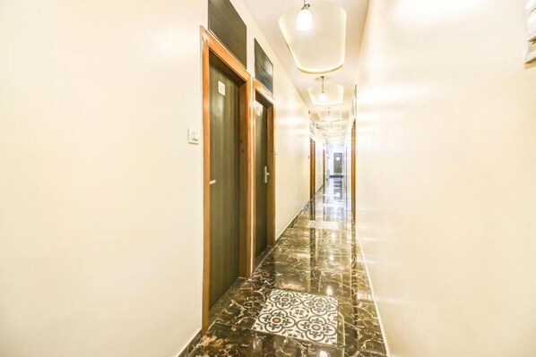 A hallway with marble flooring, wooden doors, and a modern light fixture. - New Axis By Glitz Hotels (Mumbai)
