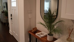 A hallway with a wooden console table, a potted plant, a mirror, and a door with a window. - Cozy Retreat in Greater Heights (Houston)