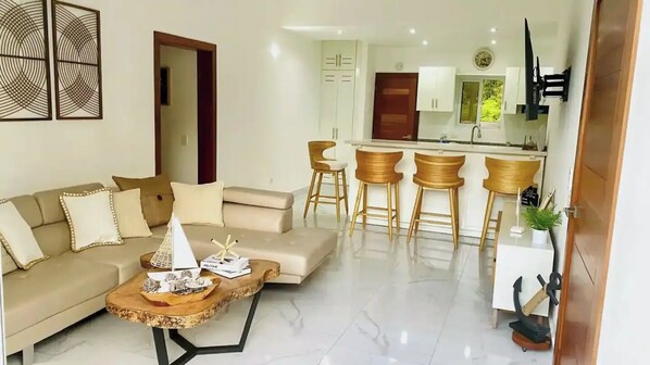 A modern living room with a sofa, coffee table, and a kitchen area with bar stools.