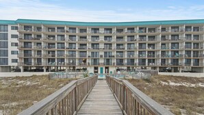 Un hôtel à plusieurs étages, doté d’une entrée principale, d’une promenade en bois menant à l’entrée et d’un parking visible au loin.