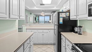 Une cuisine avec des meubles blancs, un réfrigérateur noir, une cuisinière et une vue sur l’extérieur.