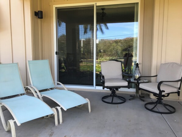 Un patio couvert comprenant deux chaises longues, une table à manger et une chaise avec un haut dossier.
