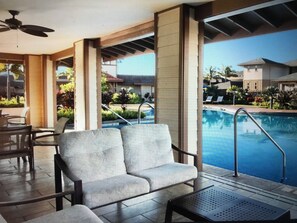Un espace aménagé au bord de la piscine, comprenant deux fauteuils rembourrés, une petite table et une piscine avec un escalier en métal.