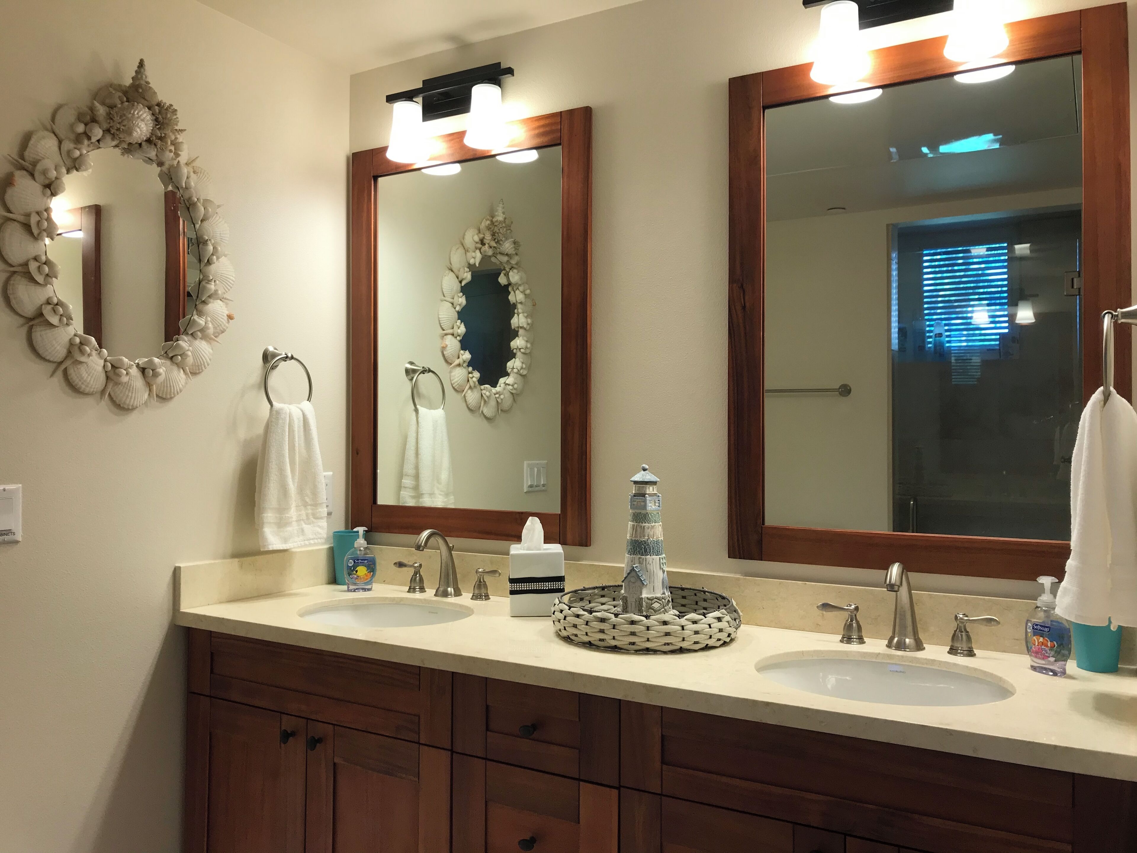 Un baño con dos lavamanos, un espejo grande y un arte decorativo de conchas.
