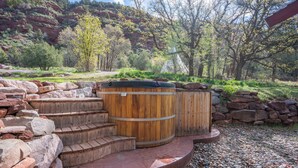 Tinaja de madera con escalones que conducen a ella, rodeada por un muro de piedra y un área de grava.