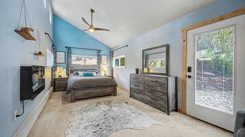 Une chambre à coucher comprenant un lit, une commode, un ventilateur de plafond et une grande fenêtre avec des stores.