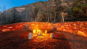 Un hogar de piedra con leña, rodeado por un muro de piedra, con montañas al fondo.