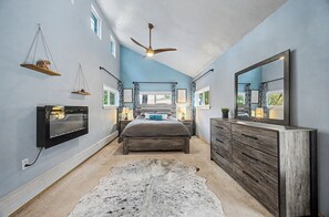 A bedroom with a bed, a ceiling fan, a mounted TV, a dresser, and a rug.