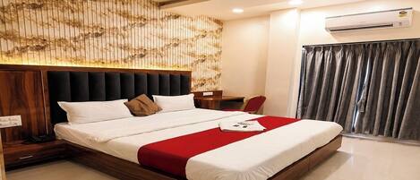 A modern hotel room with a large bed, a wooden headboard, a bedside table, and an air conditioning unit.