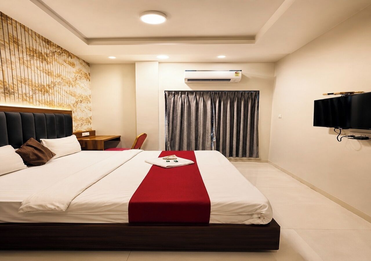 Ein Hotelzimmer mit einem großen Bett, einem Flachbildfernseher, einem Schreibtisch und einem Fenster mit Vorhängen.