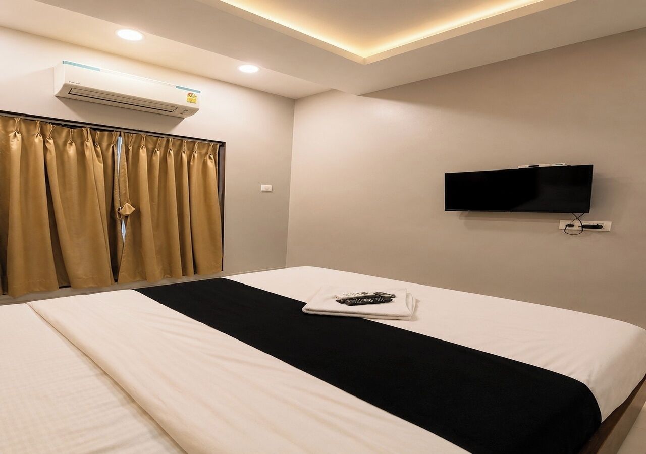 A hotel room with a bed, an air conditioning unit, a television, and curtains.