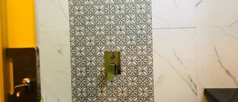 A bathroom with a patterned wall, a shower, a towel rack, and a toilet.