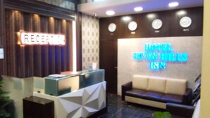 A reception area with a reception desk and a neon sign for the hotel. - New Seven Hills By Glitz Hotels (Mumbai)