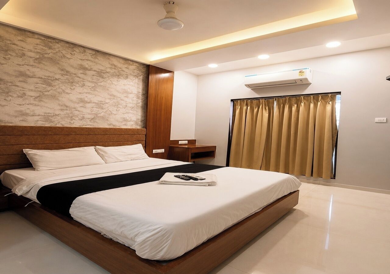 Una habitación de hotel moderna con una cama grande, cabecera de madera, mesita de noche, equipo de aire acondicionado y una ventana con cortinas.