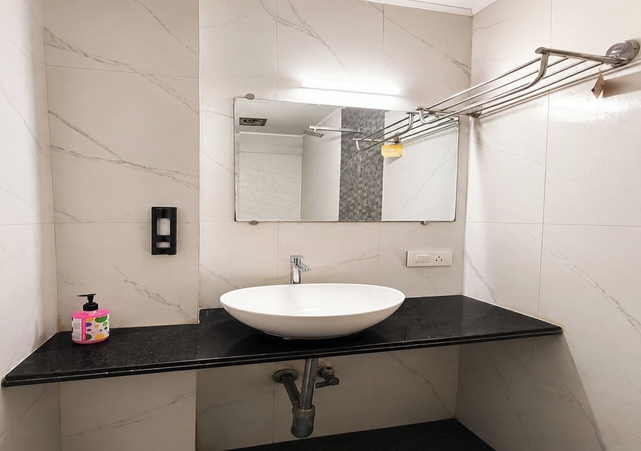 Une salle de bain avec un lavabo blanc, un plan de toilette noir et un miroir au-dessus.