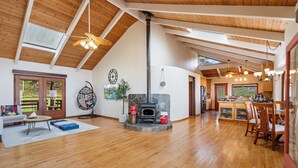 Uma sala de estar ampla com lareira de pedra, vigas de madeira no teto e uma área de jantar com cadeiras e mesa.