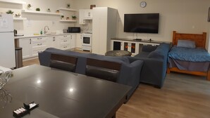 Ein zeitgemäßer Wohnraum mit Küche, Essbereich und einem Schlafzimmer mit Fernseher.