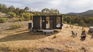 Une cabane moderne et compacte dotée d’une grande porte coulissante, d’un petit porche et d’un espace patio avec des sièges d’extérieur.