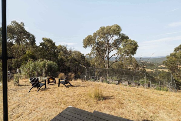 A deck with two chairs and a fire pit, surrounded by dry grass and trees.