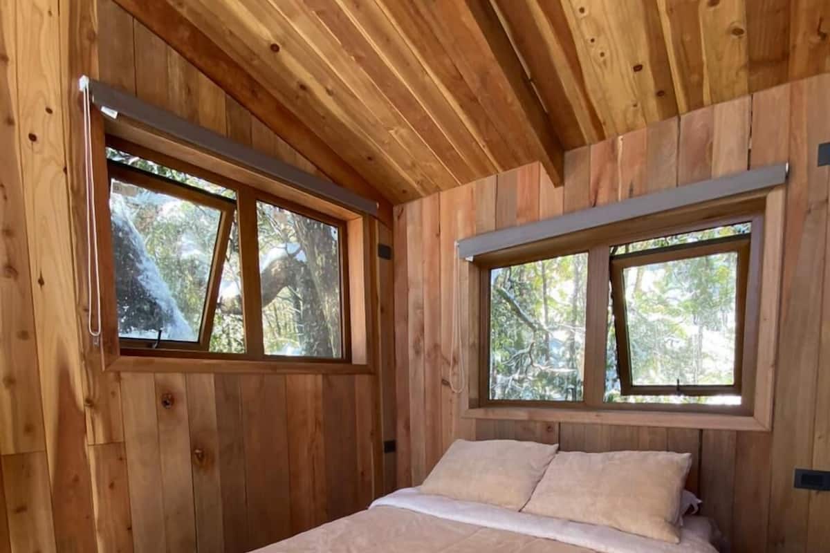 Ein Schlafzimmer in einer Holzhütte mit einem Bett, zwei Fenstern und einer Holzbalkendecke.