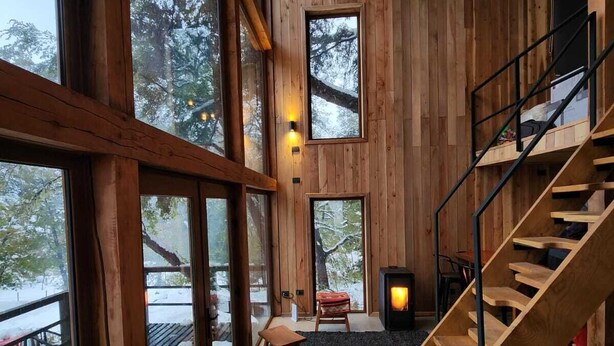 A spacious interior with large windows, a wooden staircase, and a fireplace.