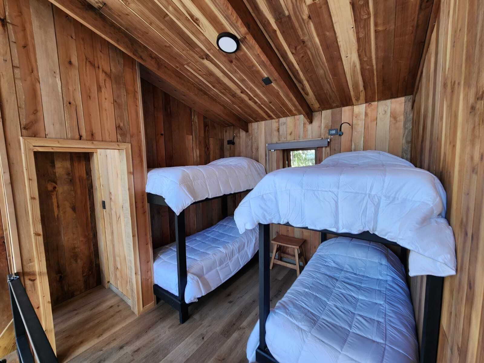 A cabin with three bunk beds, wooden walls, a small window, and a door.