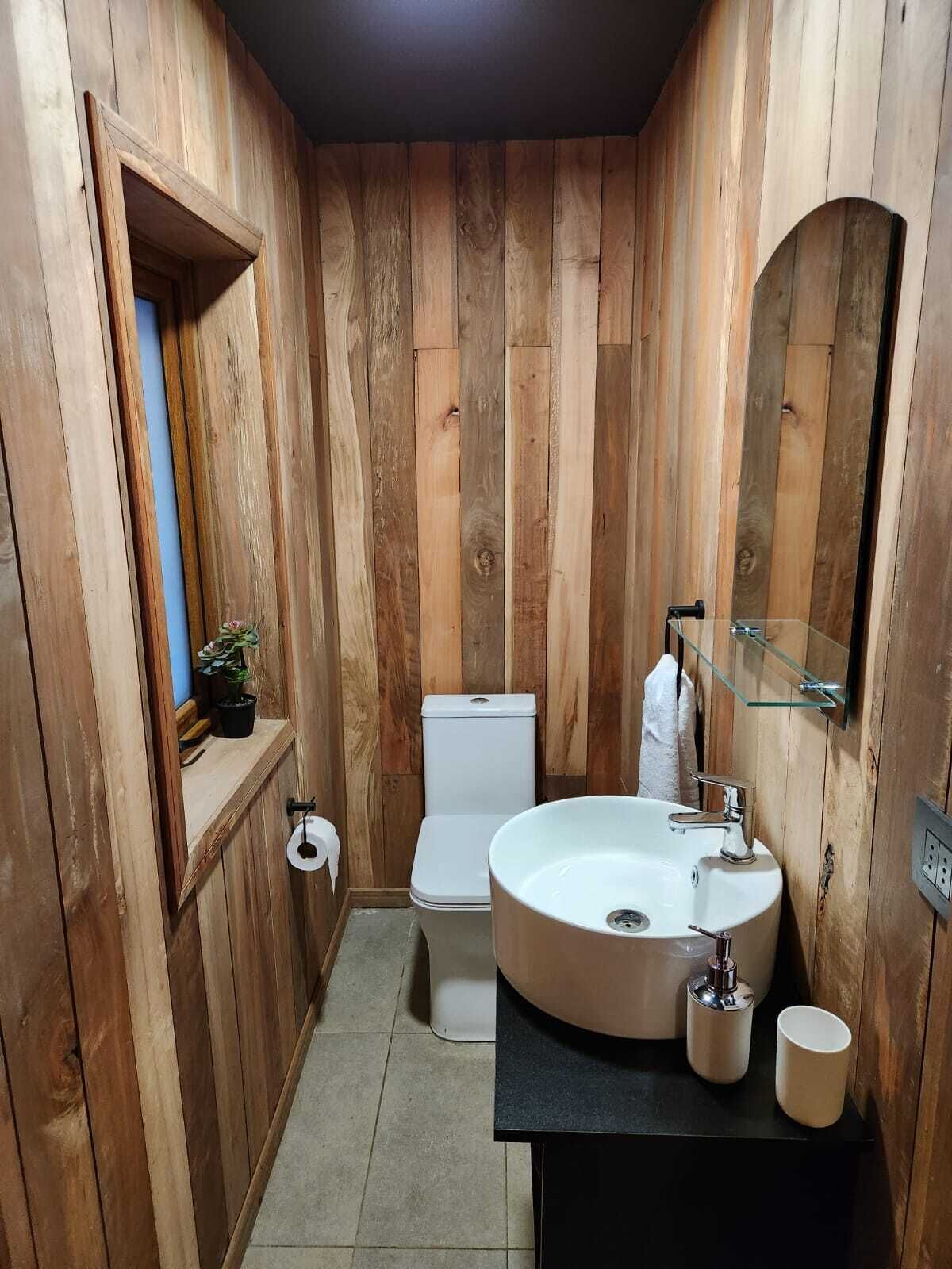 A wooden-paneled bathroom with a toilet, sink, and mirror.