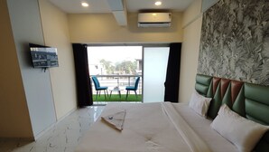 Habitación de hotel con cama, televisor montado en la pared, balcón con sillas y aire acondicionado.