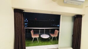 Un balcón con dos sillas, una mesita pequeña, una ventana con persianas y un equipo de aire acondicionado.