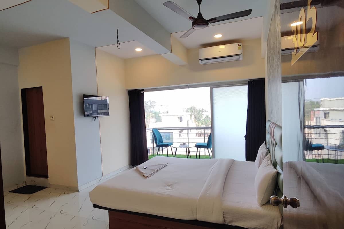 Une chambre moderne avec un grand lit, un ventilateur de plafond, un appareil de climatisation, une télévision et un balcon équipé de chaises.