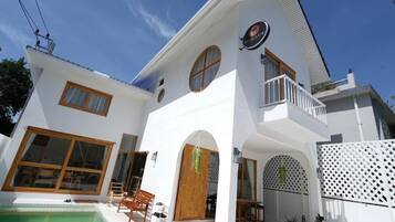 A two-story white house with a balcony, a swimming pool, and a patio area.