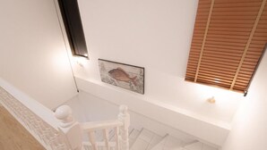 A staircase with a white railing and a wooden floor. There is a wall with a framed picture and a window with blinds. - RIM HuaHin Villa By RoomQuest (Hua Hin)