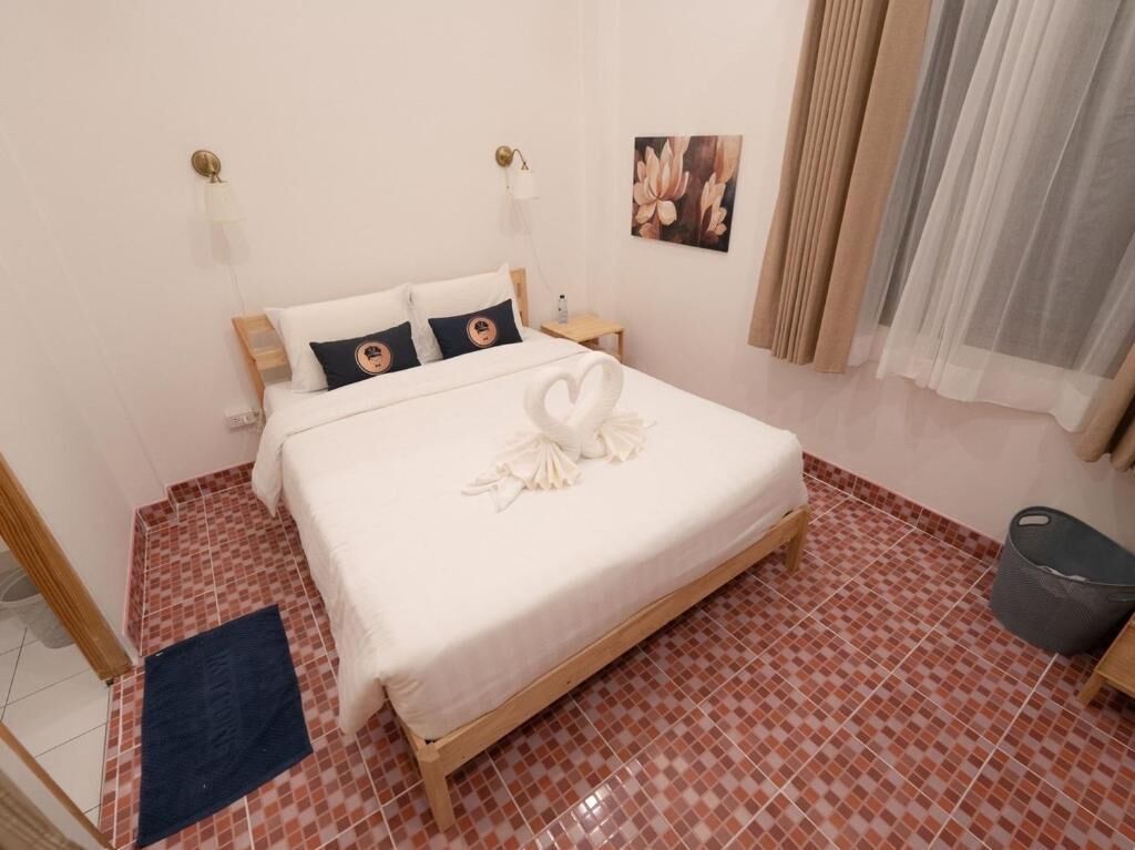 A neatly made bed with a heart-shaped towel, a small bedside table, and a wall-mounted lamp.