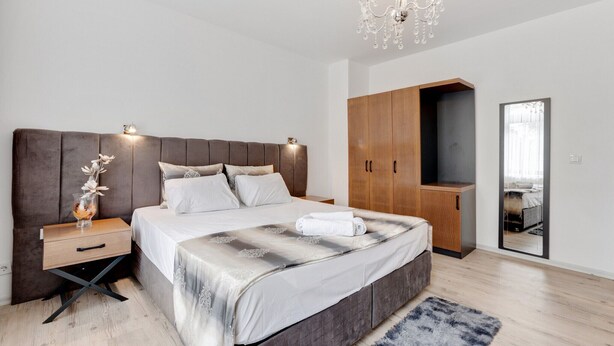 Un dormitorio moderno con una cama grande, armario de madera, mesita de noche y una araña.