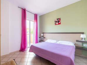 A bedroom with a bed, a nightstand, a lamp, a painting on the wall, and a sliding door with curtains.