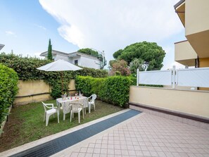 A patio area with a table and chairs, surrounded by greenery and a white fence.