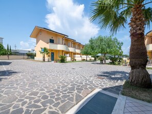 A courtyard with a paved floor, a palm tree, and a building with balconies.