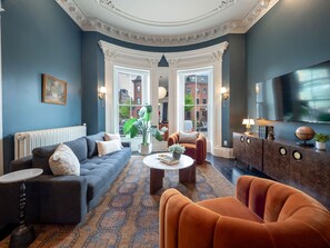 A room with a sofa, armchair, coffee table, and a cabinet with decorative items. - The Chester: Penthouse One Bedroom (Boston)