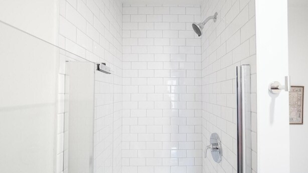 A shower with white tiles, a glass door, and a showerhead. - The Chester: Urban Chic Stay In South End (Boston)