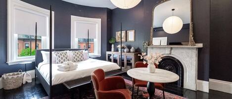 A modern bedroom with a bed, a fireplace, a round table, and a large mirror.