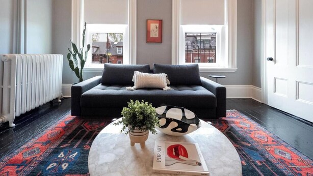 A living room with a black sofa, a round coffee table with a book and a plant, and two windows with white frames. - The Chester: Modern Luxury, Historic Charm (Boston)