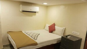 Een slaapkamer met een bed, een nachtkastje met lades, een wandairconditioner en een stopcontact.