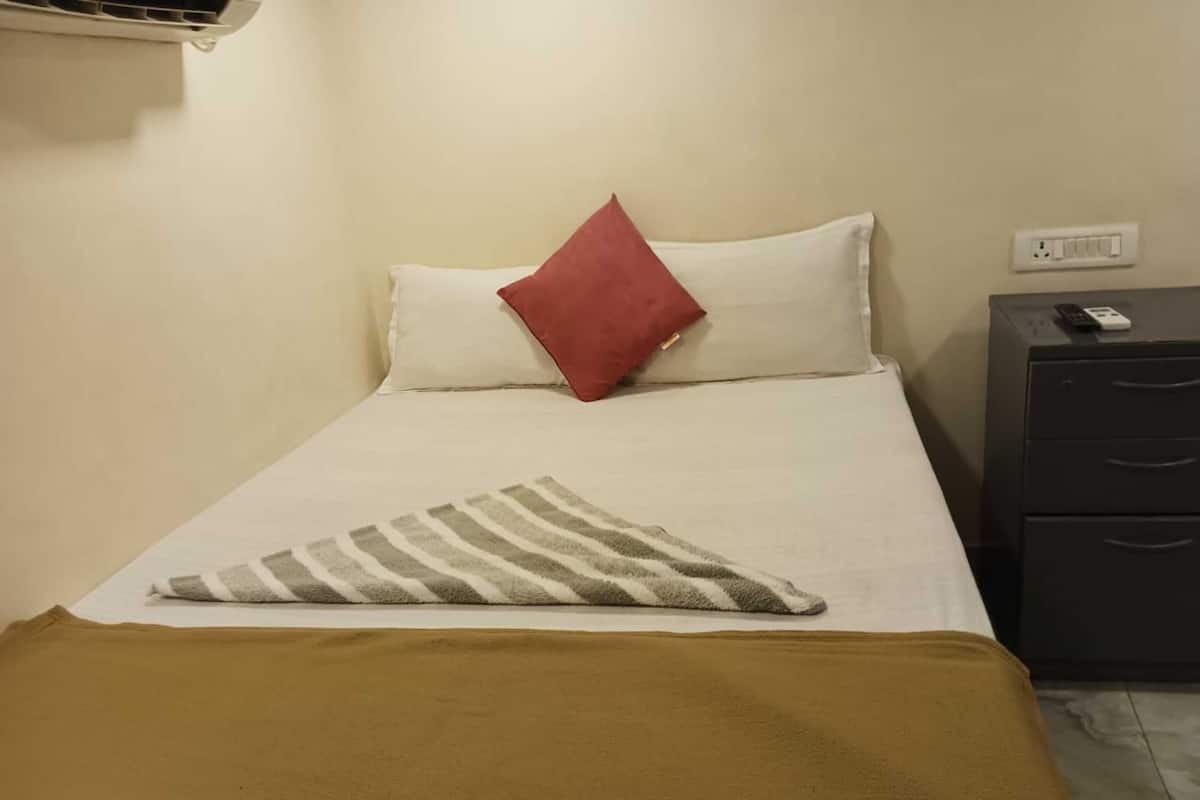 Un lit bien fait, avec une couverture rayée et un plaid marron, un oreiller rouge et un oreiller blanc sur un matelas blanc.