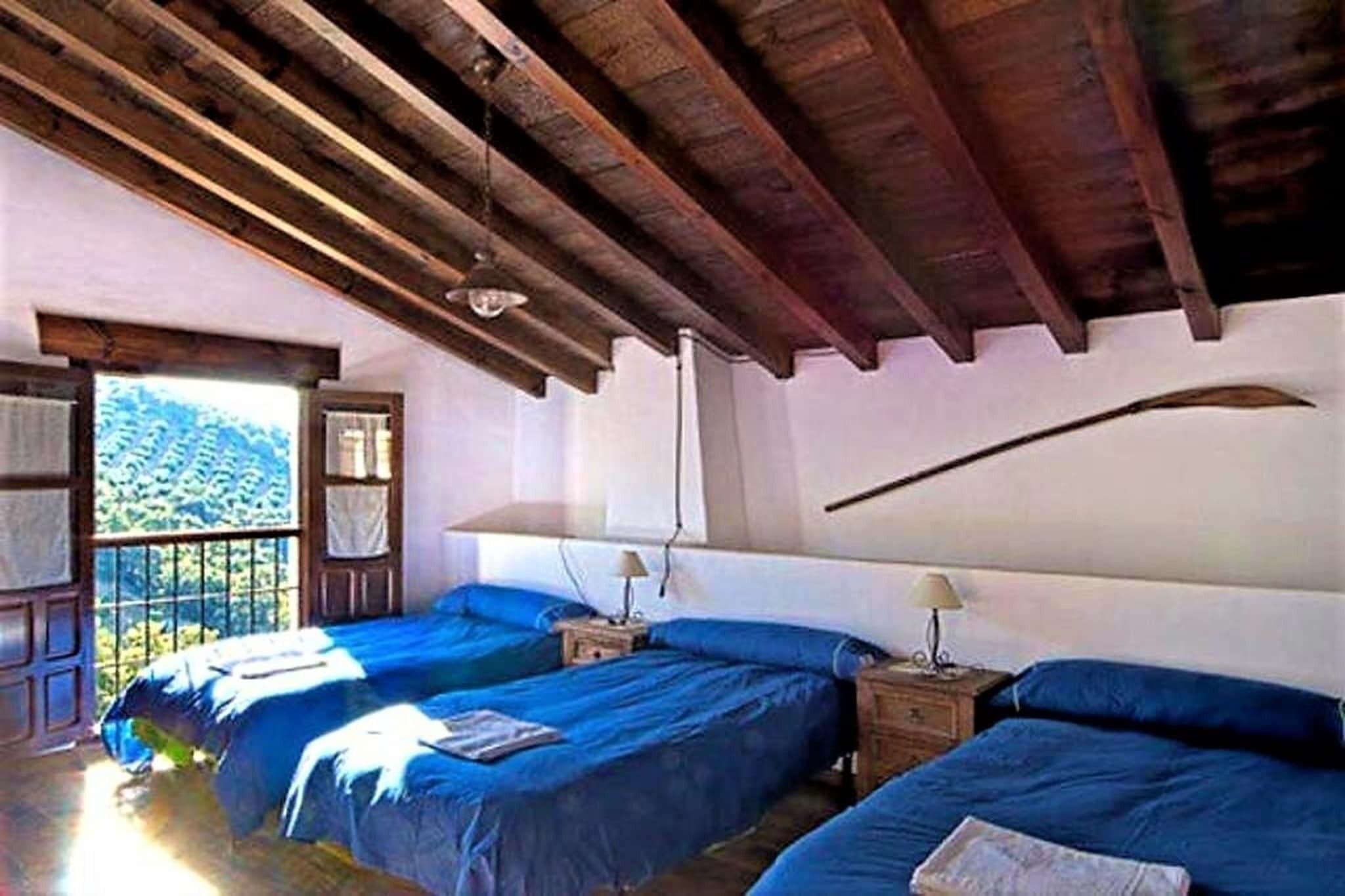 Een kamer met twee bedden, houten balken in het plafond en een raam met uitzicht op groen.