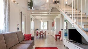 Una sala de estar moderna con un sofá, una alfombra roja y una escalera que lleva a un balcón.