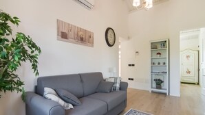 Una sala de estar con un sofá gris, un tapete estampado, un reloj de pared y una estantería.