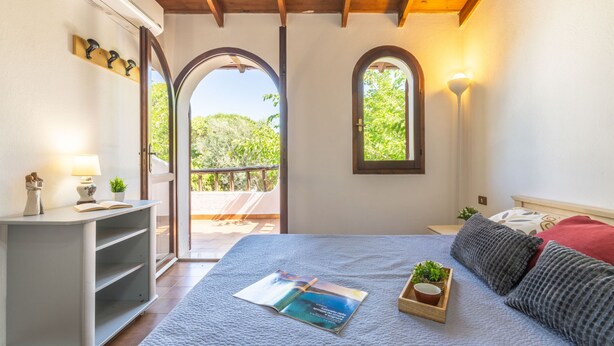 A bedroom with a bed, a bedside table with a lamp, a small shelf, and a window. - Sant'Andrea by Interhome (Capitana)