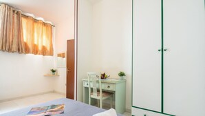 Un dormitorio con cama, escritorio, silla, armario y ventana con cortinas.