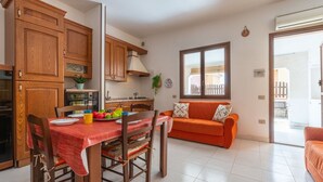 Una cocina con armarios de madera, una mesa de comedor con sillas y un sofá en una sala de estar con ventana.